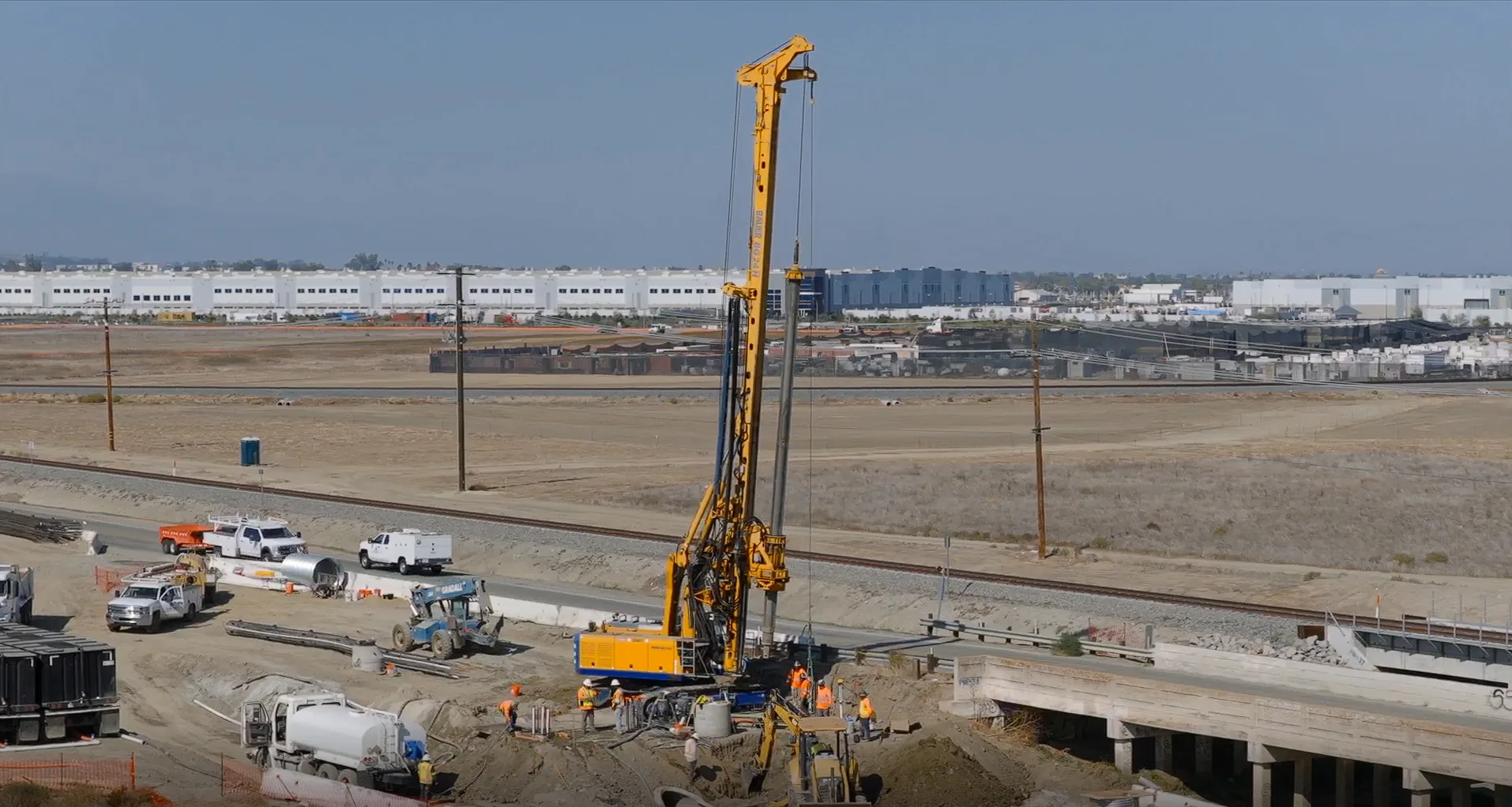 Construction crew and drill rig working alongside North Case Road with distribution centers in the background